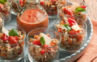Fotografia em tons de laranja em uma bancada de madeira com um pano laranja, um prato redondo desenhado verde claro com vários copinhos de vidro com a salada de grãos dentro deles e ao centro, um potinho com o molho de tomate. Fotografia em tons de laranja em uma bancada de madeira com um pano laranja, um prato redondo desenhado verde claro com vários copinhos de vidro com a salada de grãos dentro deles e ao centro, um potinho com o molho de tomate.