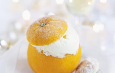 Fotografia em tons de branco com uma laranja inteira recheada de creme apoiada sobre um prato, em cima de uma mesa branca. Ao fundo, uma taça com champanhe. Fotografia em tons de branco com uma laranja inteira recheada de creme apoiada sobre um prato, em cima de uma mesa branca. Ao fundo, uma taça com champanhe.