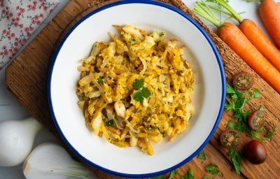 Em cima de uma mesa, prato redondo com porção de bacalhau desfiado com cebola, decorado com folha de salsa.