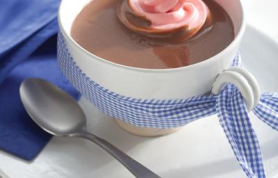 Fotografia em tons de azul em uma bancada de madeira branca com um pano azul ao lado, um prato branco raso pequeno, um xícara branca e o chocolate quente com marshmallow dentro. Fotografia em tons de azul em uma bancada de madeira branca com um pano azul ao lado, um prato branco raso pequeno, um xícara branca e o chocolate quente com marshmallow dentro.