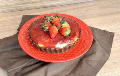 Fotografia em tons de vermelho com um prato vermelho ao centro. Em cima do prato existe um cheesecake de Galak com queijo gorgonzola, cobertura de morango e morangos inteiros Fotografia em tons de vermelho com um prato vermelho ao centro. Em cima do prato existe um cheesecake de Galak com queijo gorgonzola, cobertura de morango e morangos inteiros