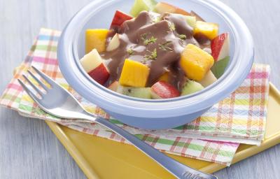 fotografia em tons de azul e cinza de uma bancada cinza vista de cima, contém um pano em tons de rosa, laranja azul e branco, um recipiente redondo e azul com frutas picadas e chocolate com raspas de limão por cima. Ao lado um garfo para servir.
