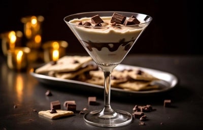 Fotografia em tons mais escuros de uma taça de vidro com a sobremesa com o creme mais claro de doce de leite, um pouco de chocolate e kitkat por cima. A taça está sobre uma mesa preta. , Fotografia em tons mais escuros de uma taça de vidro com a sobremesa com o creme mais claro de doce de leite, um pouco de chocolate e kitkat por cima. A taça está sobre uma mesa preta. ,