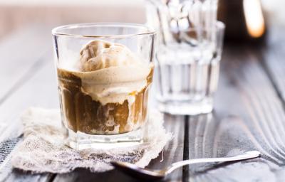 Fotografia de dois copos de vidro sobre uma mesa de madeira. O copo da frente tem uma bola de sorvete de creme com café e chocolate.