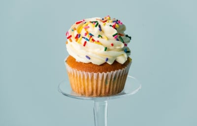 Imagem de um cupcake em forma branca decorado com chantily branco e granulados coloridos.