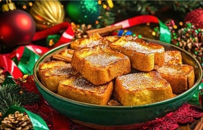 Em cima de uma mesa com bolinhas e pinhas de natal, prato com rabanadas, polvilhadas com açúcar de confeiteiro.