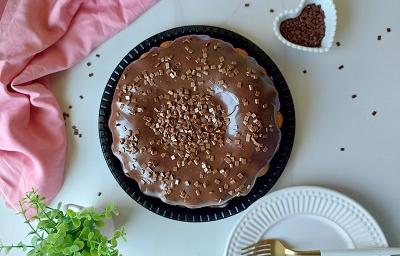 Foto em tons de marrom da receita do melhor bolo de cenoura servido sobre uma base preta com bastante cobertura de brigadeiro por cima com um paninho cor de rosa ao lado Foto em tons de marrom da receita do melhor bolo de cenoura servido sobre uma base preta com bastante cobertura de brigadeiro por cima com um paninho cor de rosa ao lado