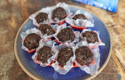 Fotografia em tons claros com um prato azul ao centro cheio de brigadeiros de palha italiana com negresco.