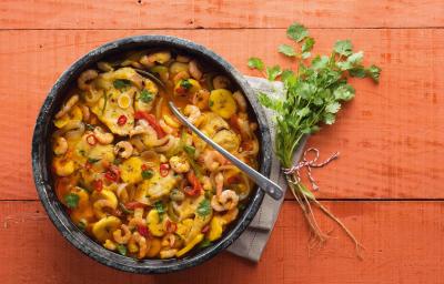 Fotografia em tons de vermelho em uma bancada de madeira vermelha com um recipiente redondo e fundo de pedra com a moqueca de peixe e camarão dentro dela. Fotografia em tons de vermelho em uma bancada de madeira vermelha com um recipiente redondo e fundo de pedra com a moqueca de peixe e camarão dentro dela.