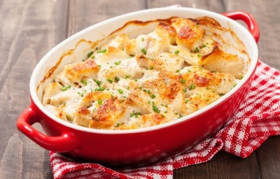 Em cima de uma mesa, refratário redondo com bacalhau gratinado com queijo, decorado com salsinha picada.