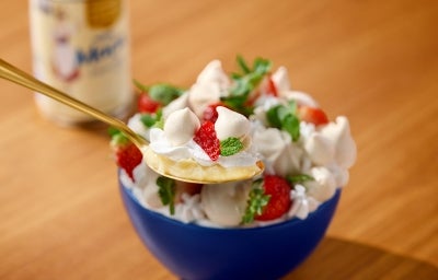 Fotografia mostra uma colherada de merengue, sendo possivel visualizar as camadas de creme, chantilly, morango e suspiro.