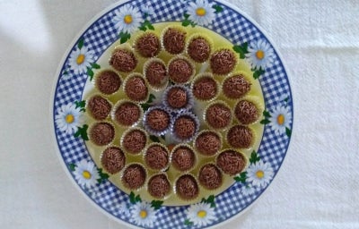 Fotografia vista de cima de várias unidades de brigadeiro enrolados e passados no granulado sobre um prato colorido, raso.