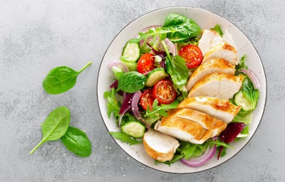 Fotografia de um peito de frango grelhado e fatiado servido em cima de uma salada de folhas e tomates