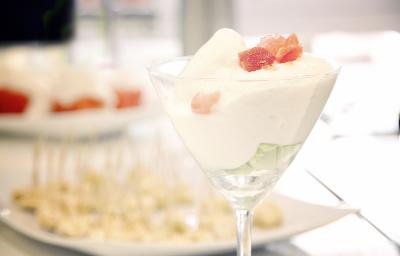 Fotografia de um sorvete de creme com champanhe e raspas de gelo em uma taça. Ao fundo, aperitivos em um recipiente de vidro na cor branco. A granita está sobre uma mesa de madeira na cor branca. Fotografia de um sorvete de creme com champanhe e raspas de gelo em uma taça. Ao fundo, aperitivos em um recipiente de vidro na cor branco. A granita está sobre uma mesa de madeira na cor branca.