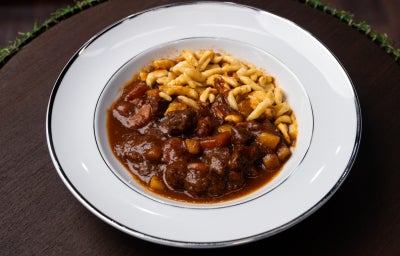Goulash com molho escuro, carne cozida lentamente e spätzle salteado no prato branco