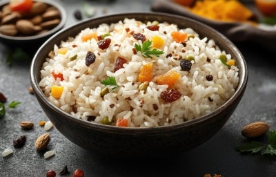 Imagme de uma tigela com arroz branco, pimentões amarelo e vermelho e uvas-passas.