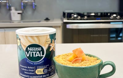 Fotografia em tons de verde e azul em uma bancada de cozinha com uma xícara verde ao centro e maçã, biscoito e canela dentro dela.