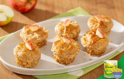 Mini cupcakes de maçã e aveia dispostos em prato branco, com pedacinhos de maçã por cima, sobre mesa de madeira.