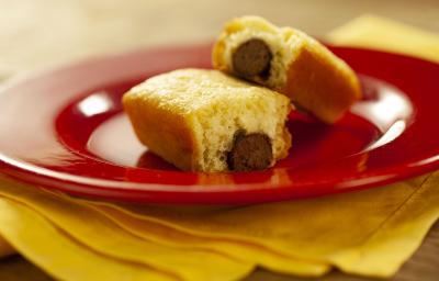 Fotografia em tons de vermelho e amarelo de uma bancada de madeira com um paninho amarelo e sobre ele um prato vermelho com dois mini bolinhos recheados com um baton. Fotografia em tons de vermelho e amarelo de uma bancada de madeira com um paninho amarelo e sobre ele um prato vermelho com dois mini bolinhos recheados com um baton.