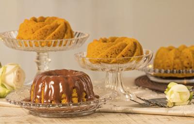 fotografia em tons de cinza, laranja e marrom vista de frente. Contém 4 bolos de cenoura e um deles esta com calda de chocolate, todos estão dentro de recipientes de vidros fotografia em tons de cinza, laranja e marrom vista de frente. Contém 4 bolos de cenoura e um deles esta com calda de chocolate, todos estão dentro de recipientes de vidros
