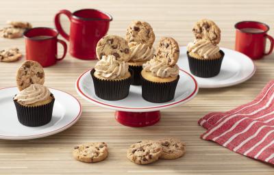 Foto de uma bancada clara com canecas e um bule vermelhos, um tecido listrado vermelho e branco. Há dois pratos brancos com cupcakes em cima e, ao centro, um prato com três cupcakes decorados com cookies. Foto de uma bancada clara com canecas e um bule vermelhos, um tecido listrado vermelho e branco. Há dois pratos brancos com cupcakes em cima e, ao centro, um prato com três cupcakes decorados com cookies.