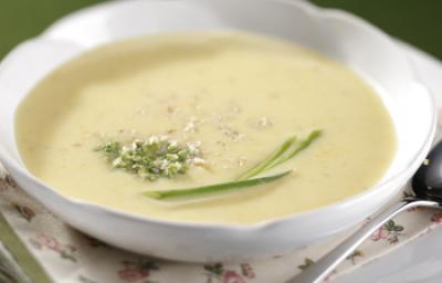 Fotografia em tons de verde em uma bancada com uma bandeja branca, um pano branco com detalhes verde e em flores, um prato redondo branco fundo em cima dela e o creme de mandioquinha. Fotografia em tons de verde em uma bancada com uma bandeja branca, um pano branco com detalhes verde e em flores, um prato redondo branco fundo em cima dela e o creme de mandioquinha.