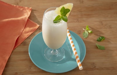 Foto da receita de pina colada feita com novasource proline servida em um copo de vidro para drinks com um canudo listrado ao lado sobre um prato azul claro Foto da receita de pina colada feita com novasource proline servida em um copo de vidro para drinks com um canudo listrado ao lado sobre um prato azul claro