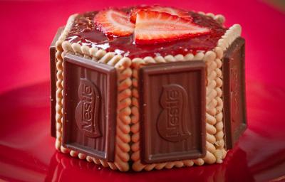 Fotografia em tons de vermelho com uma sobremesa ao centro. Essa sobremesa é feita por camadas laterias de biscoito de chocolate Choco Biscuit e finalizadas com geleia de morango no topo