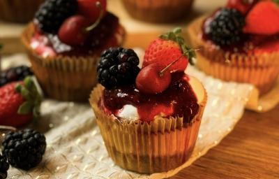 Fotografia de uma mini cheesecake com frutas vermelhas feita em uam forminha de papel de cupcake, ao fundo tem mais algumas. Fotografia de uma mini cheesecake com frutas vermelhas feita em uam forminha de papel de cupcake, ao fundo tem mais algumas.