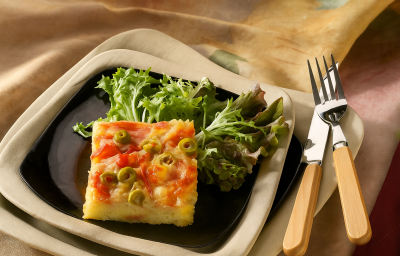 Imagem de um prato quadrado com o pedaço da torta com azeitonas e ovos e ao lado salada de folhas verdes.