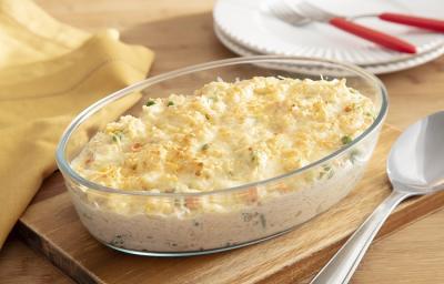 Foto da Receita de Arroz de Forno Cremoso com Sobras de Frango e Seleta de Legumes. Observa-se um refratário de vidro oval com o arroz gratinado e, ao lado, uma colher de servir de inox.