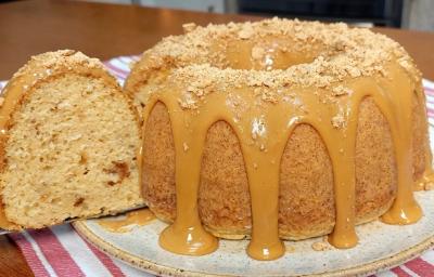 Foto em tons de caramelo da receita de bolo de paçoca com leite ninho servida em uma porção inteira com um pedaço cortado sobre uma base de cerâmica em cima de um paninho listrado rosa Foto em tons de caramelo da receita de bolo de paçoca com leite ninho servida em uma porção inteira com um pedaço cortado sobre uma base de cerâmica em cima de um paninho listrado rosa