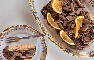 Fotografia em tons de brano com uma travessa de vidro ao centro. Em cima da travessa existe uma receita de Choco Torta coberta com raspas de chocolate ao leite e pedaços de laranja Fotografia em tons de brano com uma travessa de vidro ao centro. Em cima da travessa existe uma receita de Choco Torta coberta com raspas de chocolate ao leite e pedaços de laranja