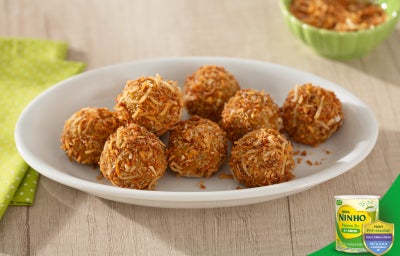 Trufas de cenoura com uva-passa em formato de bolinhas, cobertas com coco ralado, dispostas em prato branco sobre mesa clara.