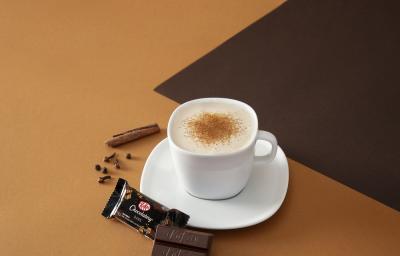 Foto da receita de cappuccino chai cremoso servida em uma xícara branca com um kit kat dark ao lado em fundo marrom claro e escuro