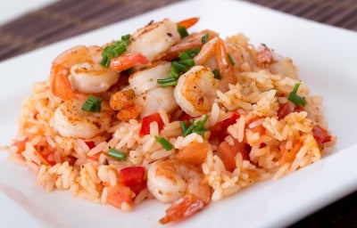 Prato branco quadrado com porção de arroz cremoso e camarão com pimentão vermelho picados.