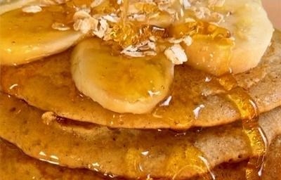 Fotografia cinco panquecas de baunilha empilhadas com mel, banana em rodelas e aveia por cima. As panquecas estão sobre um prato de vidro branco. Fotografia cinco panquecas de baunilha empilhadas com mel, banana em rodelas e aveia por cima. As panquecas estão sobre um prato de vidro branco.