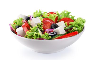 fotografia em tons de branco, verde, vermelho e preto tirada de um recipiente redondo branco com folhas de alface, fatias de tomates, queijo em cubo e fatias de azeitonas pretas.