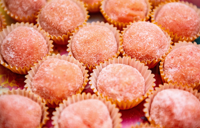 Fotografia de vários docinhos de cor rosa em pequenas forminhas. Cada um dos docinhos está polvilhado com açúcar Fotografia de vários docinhos de cor rosa em pequenas forminhas. Cada um dos docinhos está polvilhado com açúcar