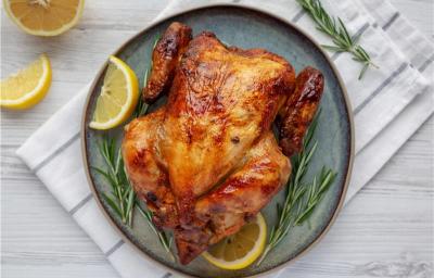 A imagem mostra um frango assado disposto em um prato azul com rodelas de limão e alecrim A imagem mostra um frango assado disposto em um prato azul com rodelas de limão e alecrim
