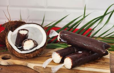 Fotografia de geladinhos em sacos plásticos com cobertura de chocolate e creme de coco branco por dentro. Ao lado cocos decorativos. Fotografia de geladinhos em sacos plásticos com cobertura de chocolate e creme de coco branco por dentro. Ao lado cocos decorativos.