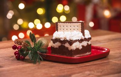 Fotografia de um bolo com três camadas com chantilly e um biscoito no topo. O bolo está sobre um prato vermelho.