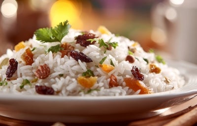 Prato de arroz branco, soltinho, com uma textura leve e fofa com uvas-passas pretas, decorado com folha de coentro.