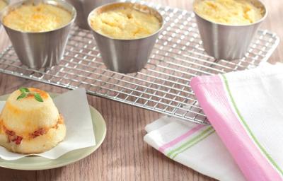 contém 4 potinhos redondos de alumínio com a massa dentro todos por cima de uma grade. Um prato redondo verde com o Muffin e ao lado um pano em tons de branco, rosa e verde. contém 4 potinhos redondos de alumínio com a massa dentro todos por cima de uma grade. Um prato redondo verde com o Muffin e ao lado um pano em tons de branco, rosa e verde.