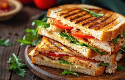 imagem mostra um sanduiche com camadas de creme de frango, folhas de alface e rodelas de tomate em um pão de forma