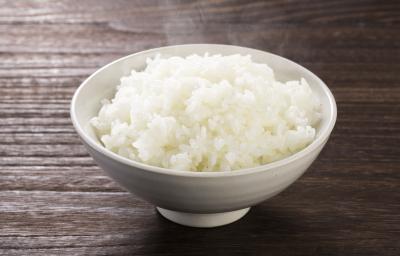 Fotografia em tons de marrom e branco de uma bancada de madeira vista de cima, um recipiente branco redondo contém arroz branco dentro. Fotografia em tons de marrom e branco de uma bancada de madeira vista de cima, um recipiente branco redondo contém arroz branco dentro.