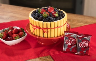 Fotografia em tons de vermelho com um bolo decorado com KitKat mystery, o biscoito kitkat de cor amarela. O bolo possui diversas frutas vermelhas no topo. Fotografia em tons de vermelho com um bolo decorado com KitKat mystery, o biscoito kitkat de cor amarela. O bolo possui diversas frutas vermelhas no topo.