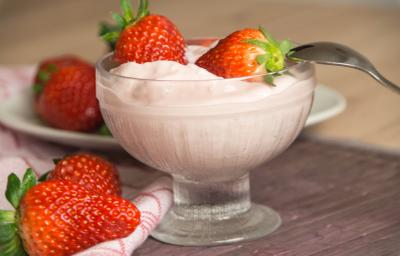 Fotografia de um creme de frutas vermelhas com iogurte, sobre o gelado, dois morangos inteiros e uma colher apoiada no recipiente de vidro em que está o creme. Ao lado, dois morangos, e ao fundo, mais morangos em cima de um prato branco pequeno. Fotografia de um creme de frutas vermelhas com iogurte, sobre o gelado, dois morangos inteiros e uma colher apoiada no recipiente de vidro em que está o creme. Ao lado, dois morangos, e ao fundo, mais morangos em cima de um prato branco pequeno.
