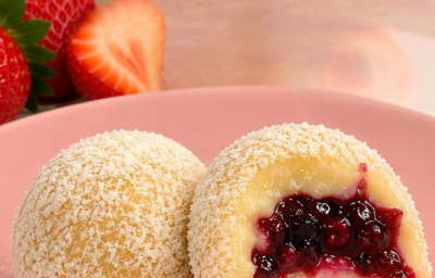 Fotografia em tons rosas com dois brigadeiros de ninho com frutas vermelhas ao centro, um dos brigadeiros está mordido.