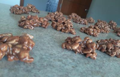Foto em tons de marrom da receita de pé de moleque com nescau servida em diversas porções sobre uma bancada de mármore escura